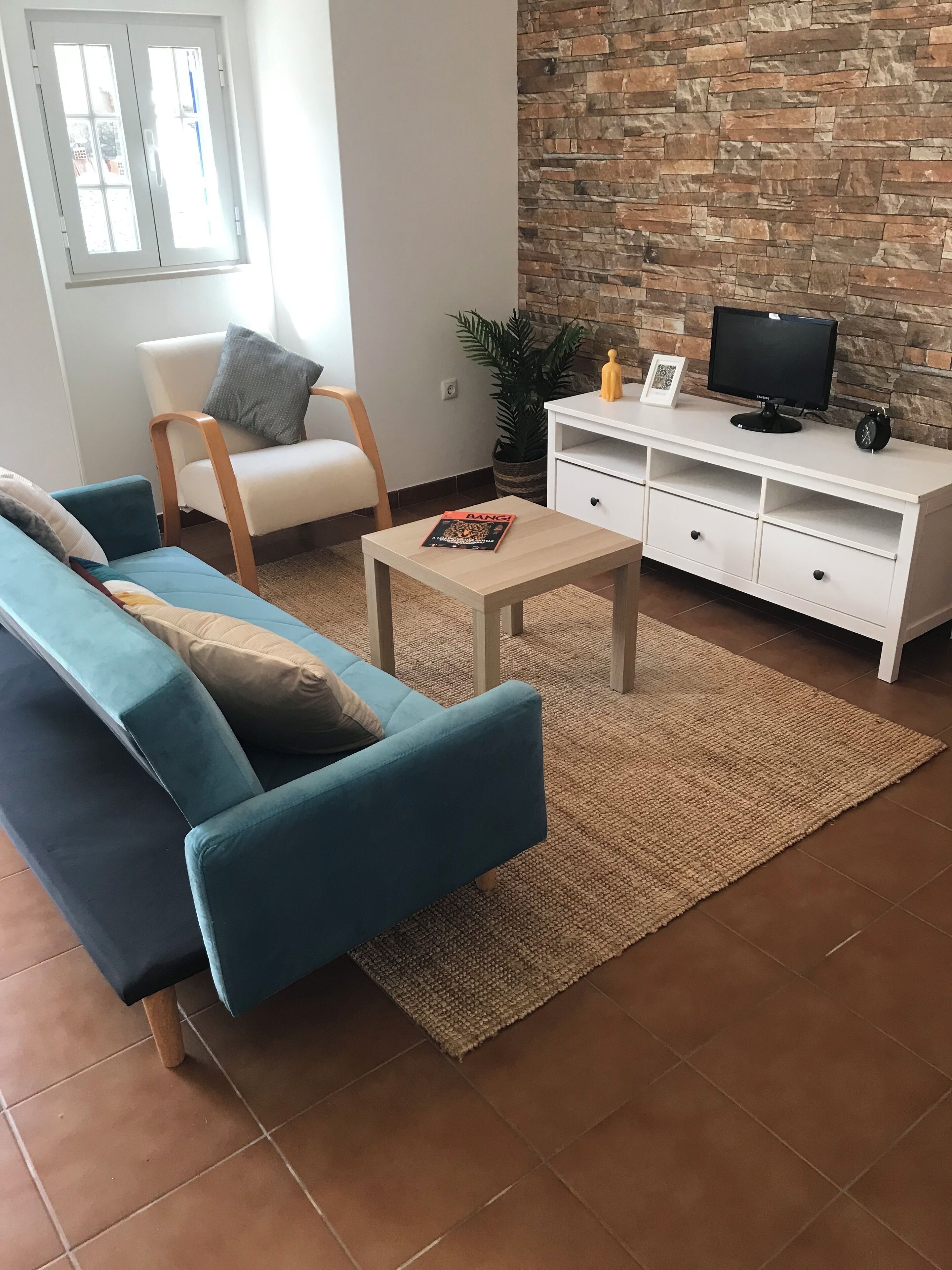 A living room with a blue sofa, a white armchair, a coffee table, and a TV on a white cabinet.