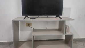 Ein Flachbildfernseher auf einem weißen, minimalistischen Standfuß, verbunden mit einem Kabel.