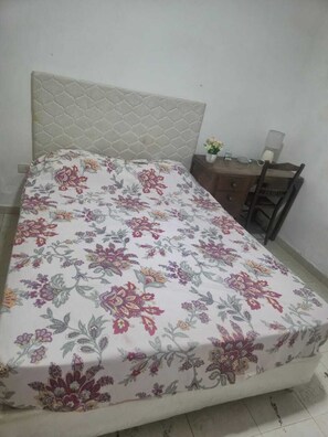 A bed with a floral bedspread, a headboard, a nightstand with a lamp, and a chair.
