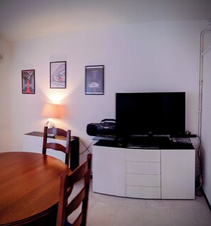 A small, compact living space with a dining table, a TV, and a printer on a white cabinet. - 6-bed apartment with private garage (Nîmes)