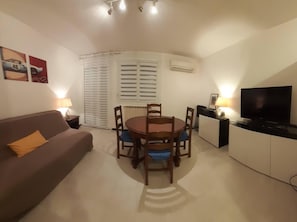 A compact living space with a dining table, a sofa, a TV, and a kitchenette. - 6-Bedroom Apartment with Private Garage (Nîmes)