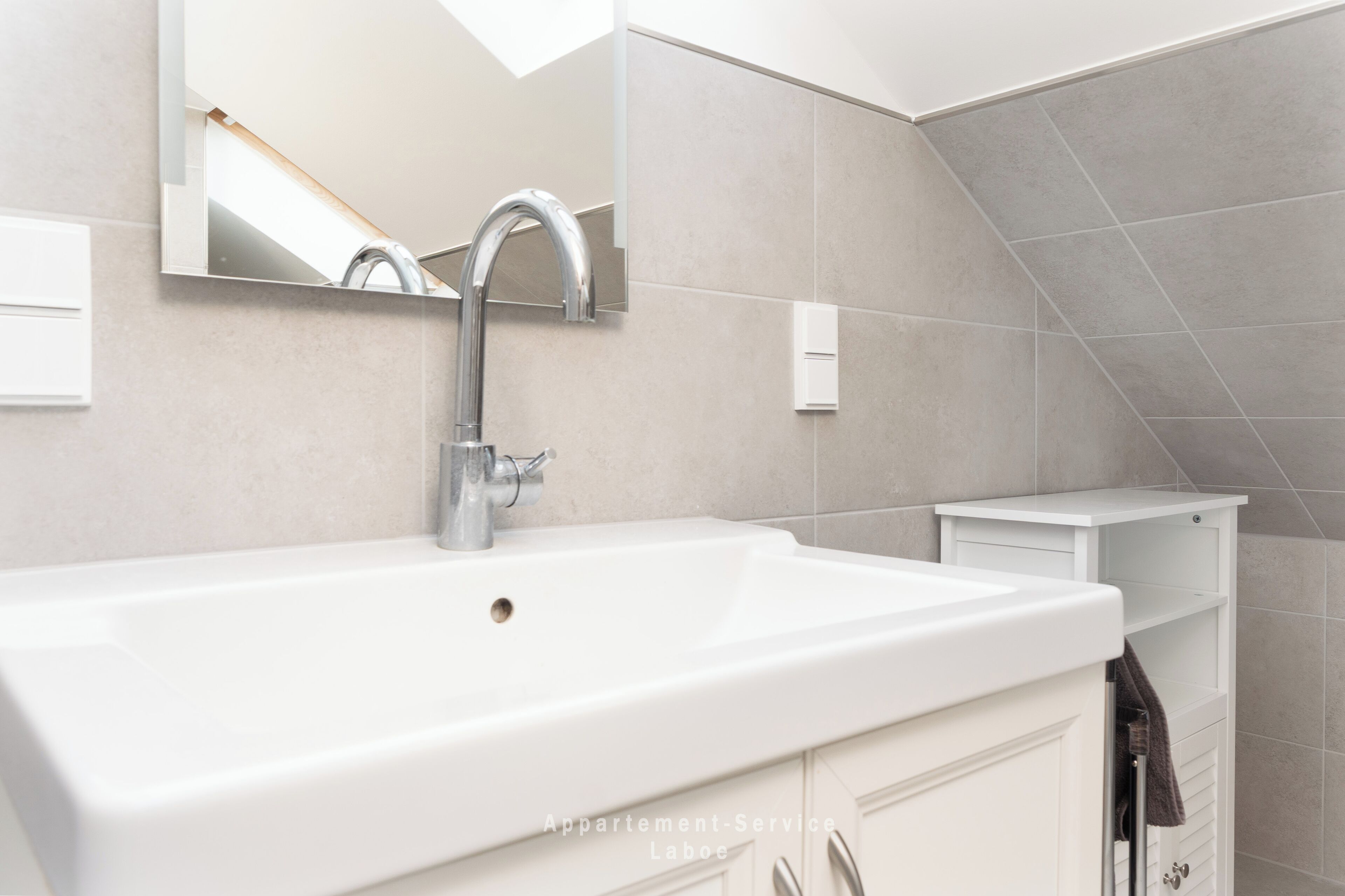 Een moderne badkamer met een grote witte wastafel, een spiegel en een handdoekhouder.
