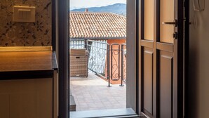 Una porta aperta che dà su un balcone con tetto in tegole, un cesto di vimini e una ringhiera in metallo.