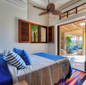 Un dormitorio con una cama, contraventanas de madera, un ventilador de techo y vistas al exterior.