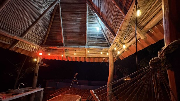 Ein Essbereich im Freien mit Holztisch und -stühlen, einer Hängematte und einer Decke mit Lichterketten.