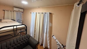 Ein kleines, gemütliches Zimmer mit einem Bett, einem Sessel, einem Teleskop und einem Vorhang.