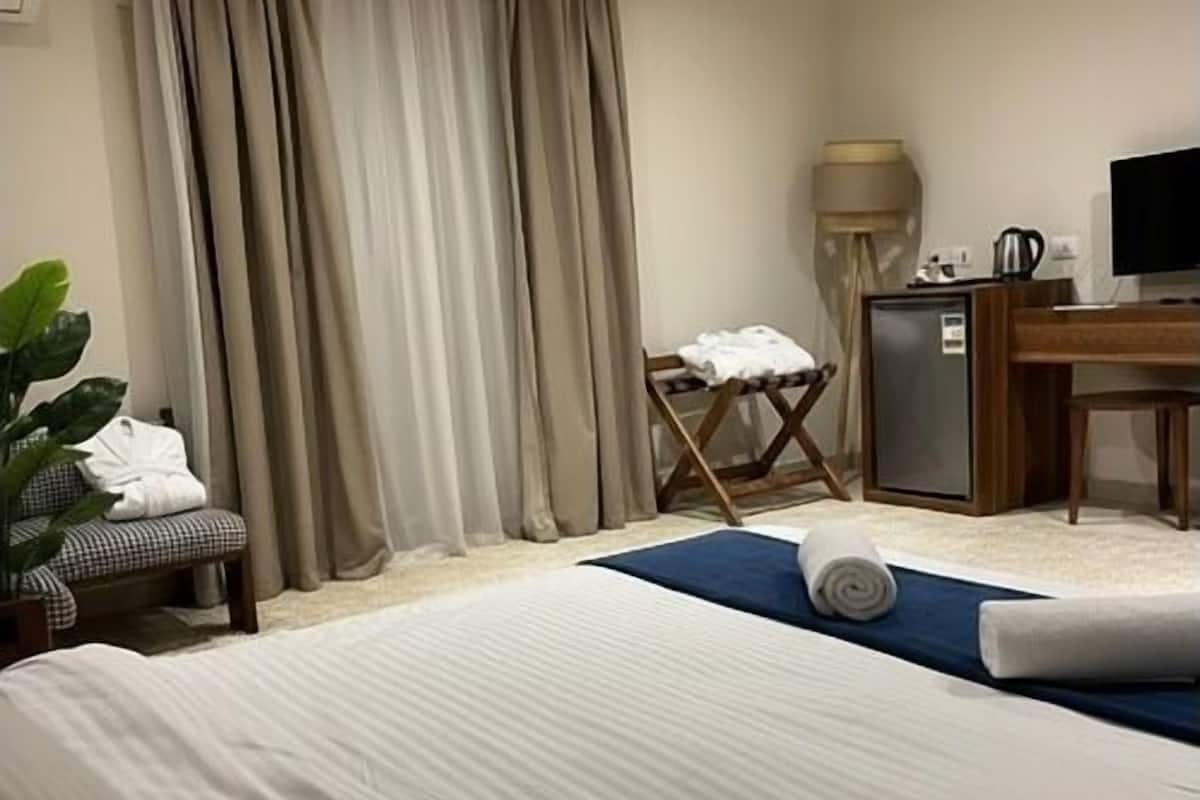 Una habitación de hotel con cama, escritorio, silla, televisor y un refrigerador pequeño.
