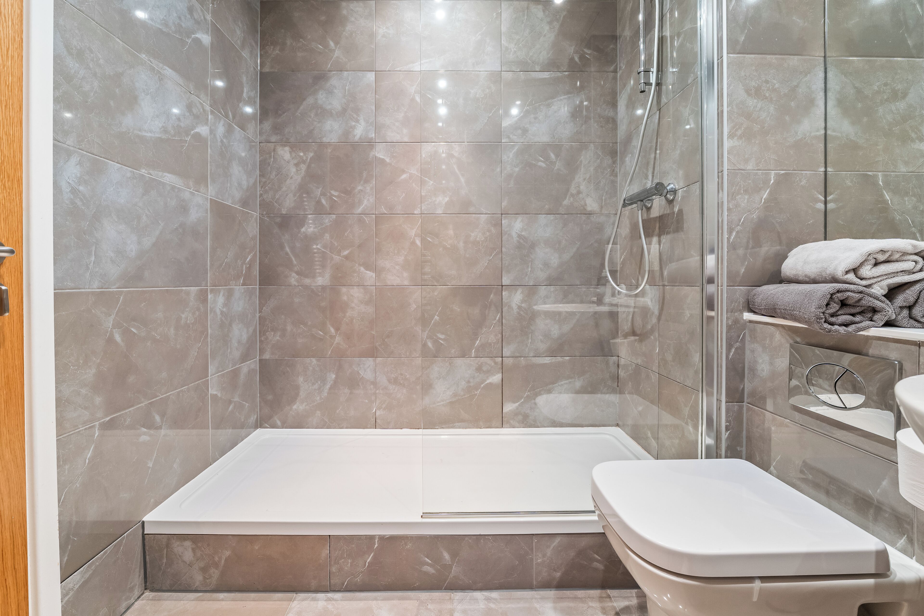 A modern bathroom with a glass-enclosed shower, a white bathtub, and a toilet.
