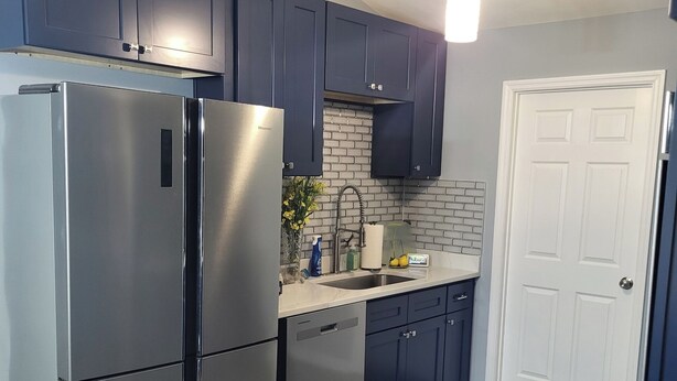 A modern kitchen with dark blue cabinets, stainless steel appliances, a white door, and a wooden floor. - The Fields Master's Rental 2026 (Augusta)