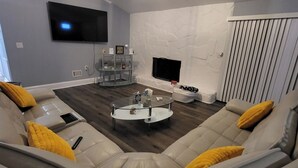 A modern living room with a sectional sofa, a glass coffee table, a flat-screen TV, and a fireplace. - The Fields Master's Rental 2026 (Augusta)