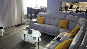 A modern living room with a grey sectional sofa, a glass coffee table, and a dining area in the background. - The Fields Master's Rental 2026 (Augusta)