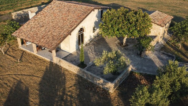 An aerial view of a rustic stone building with a tiled roof, surrounded by a garden with various shrubs and a small tree. - Ancient cottage nestled in the heart of the Sicilian countryside just a few steps from the sea (Partinico)