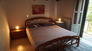 A bedroom with a wooden bed, two bedside tables with lamps, a radiator, and a window with a view of greenery. - Ancient cottage nestled in the heart of the Sicilian countryside just a few steps from the sea (Partinico)