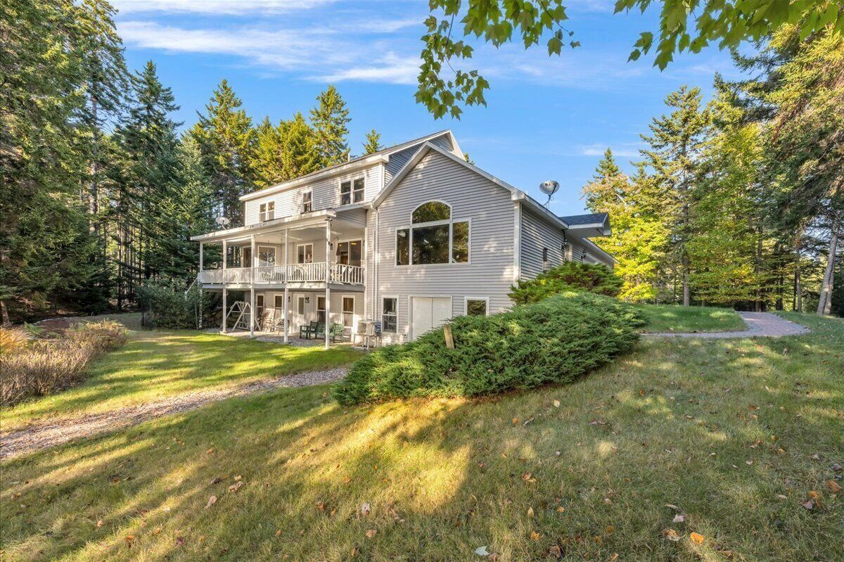 Une maison à deux étages dotée d’un porche, entourée d’une pelouse bien entretenue et d’arbres touffus.