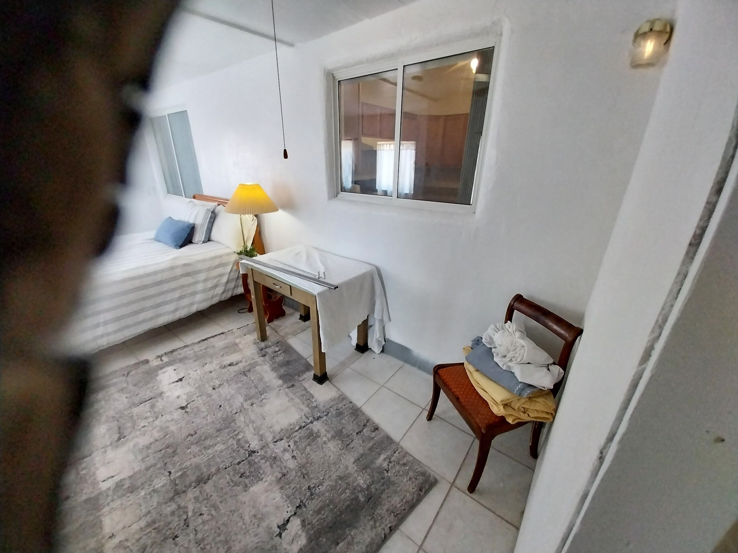 A bedroom with a bed, a desk, a chair, a lamp, and a window.