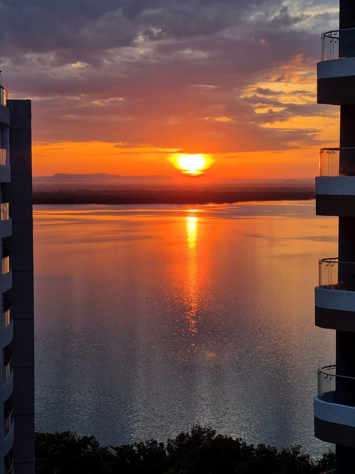 A sunset over a calm body of water with a building on the left.