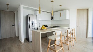 A modern kitchen with a central island, stainless steel refrigerator, and wooden chairs. - Apartamento familiar en Cartagena, cerca al aeropuerto y playa Las Americas (cartagena de indias)
