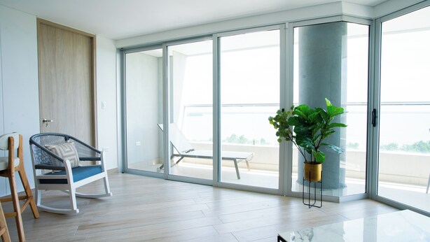 A spacious room with a sliding glass door leading to a balcony, a white chair, and a potted plant. - Apartamento familiar en Cartagena, cerca al aeropuerto y playa Las Americas (cartagena de indias)