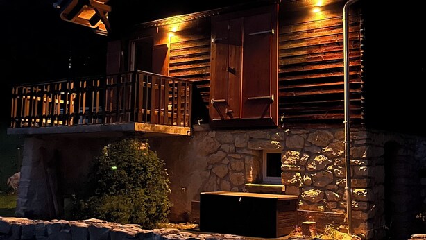 A log cabin with a stone foundation, wooden exterior, and a porch with a railing. - Comfortable chalet in the heart of the Bernese Jura (Valbirse)