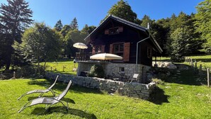 A rustic chalet with a stone foundation, wooden shutters, and a balcony with umbrellas. - Comfortable chalet in the heart of the Bernese Jura (Valbirse)