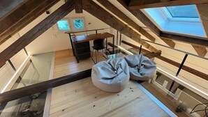 A loft-style room with a high ceiling, wooden beams, a skylight, a glass railing, and a desk with a chair. - Comfortable chalet in the heart of the Bernese Jura (Valbirse)