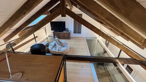 An attic bedroom with a sloped ceiling, wooden beams, a bed, a small table with a TV, and a window. - Comfortable chalet in the heart of the Bernese Jura (Valbirse)