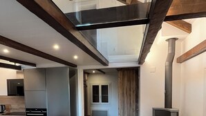 A modern kitchen with built-in appliances, a dining area with a wooden table and chairs, and a fireplace. - Comfortable chalet in the heart of the Bernese Jura (Valbirse)