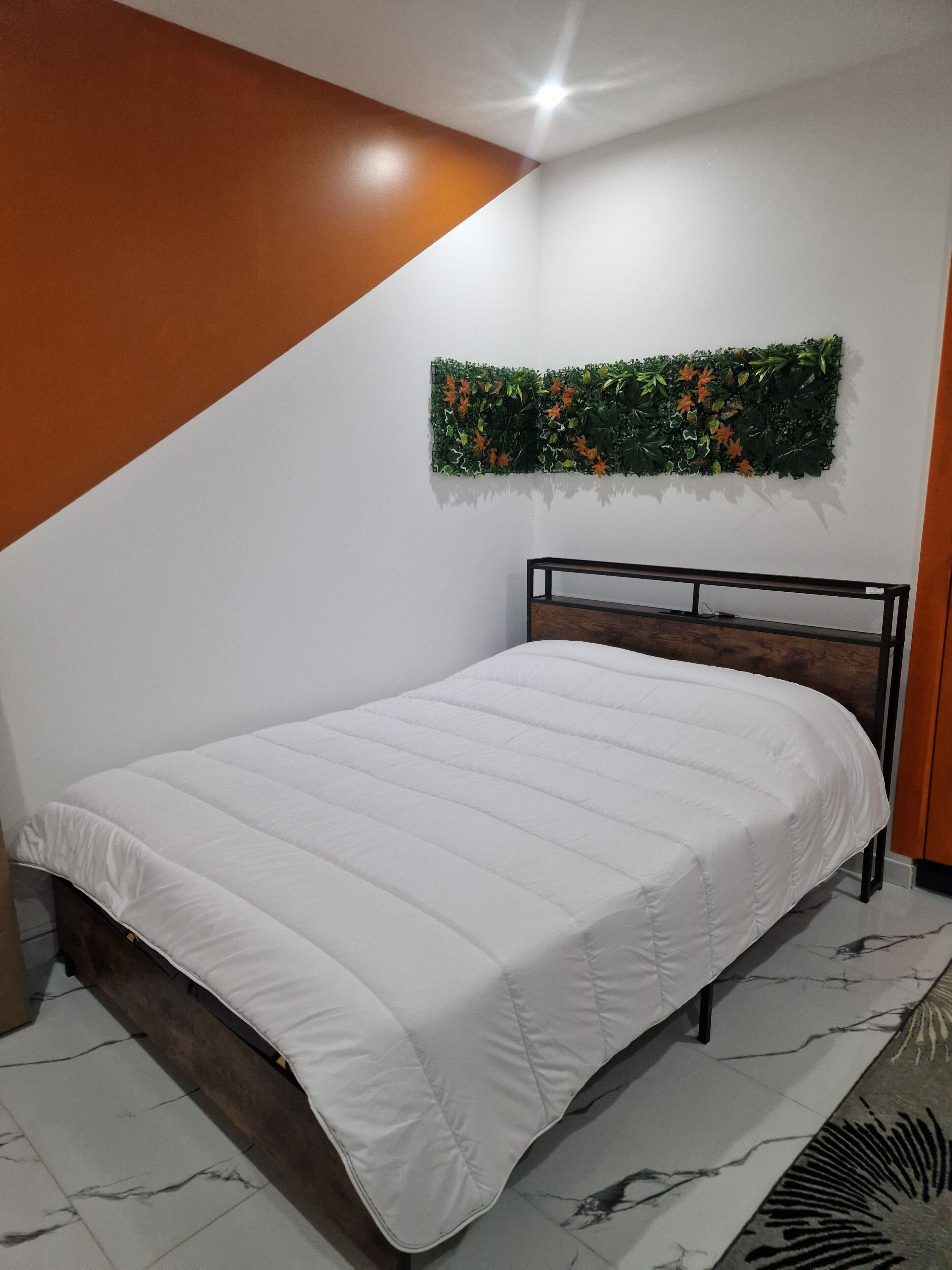 A neatly made bed with a white duvet in a modern room with a wooden headboard and a decorative wall hanging.