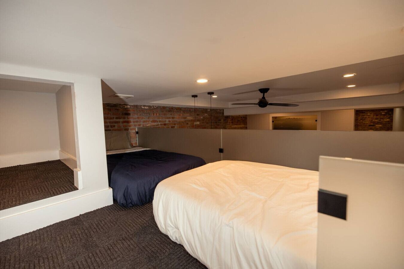 Een hotelkamer met een bed, een bureau, een plafondventilator en een bakstenen muur.