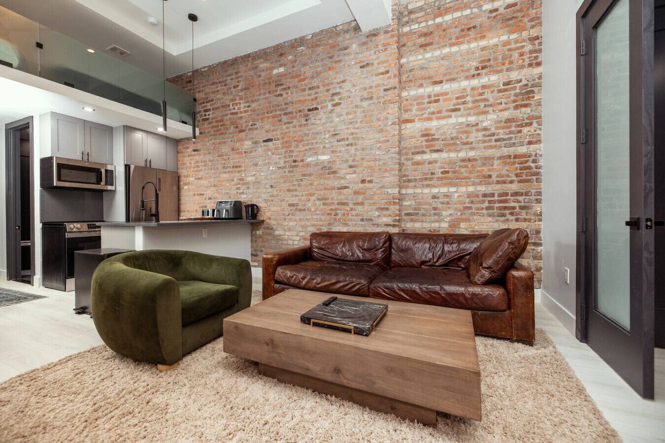 Una sala moderna con pared de ladrillo, un sofá de cuero, un sillón verde y una mesa de centro de madera.