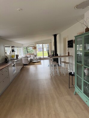 A modern kitchen with a dining area, white cabinetry, and a green cabinet with glass doors. - Modernised cottage near woods and beach (Allingåbro)