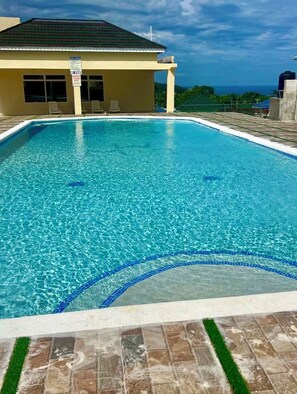 A rectangular swimming pool with clear blue water, surrounded by a tiled deck and a building with a tiled roof. - Ocho Rios home "Elevate Escape" Gated Community (Ocho Rios)