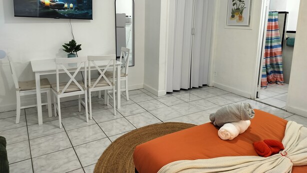 Moderni hotellihuone, jossa on ruokailutila, televisio, jossa näkyy Buddhan patsas, peili, liukuovi ja sänky, jonka päällä on pehmolelu.