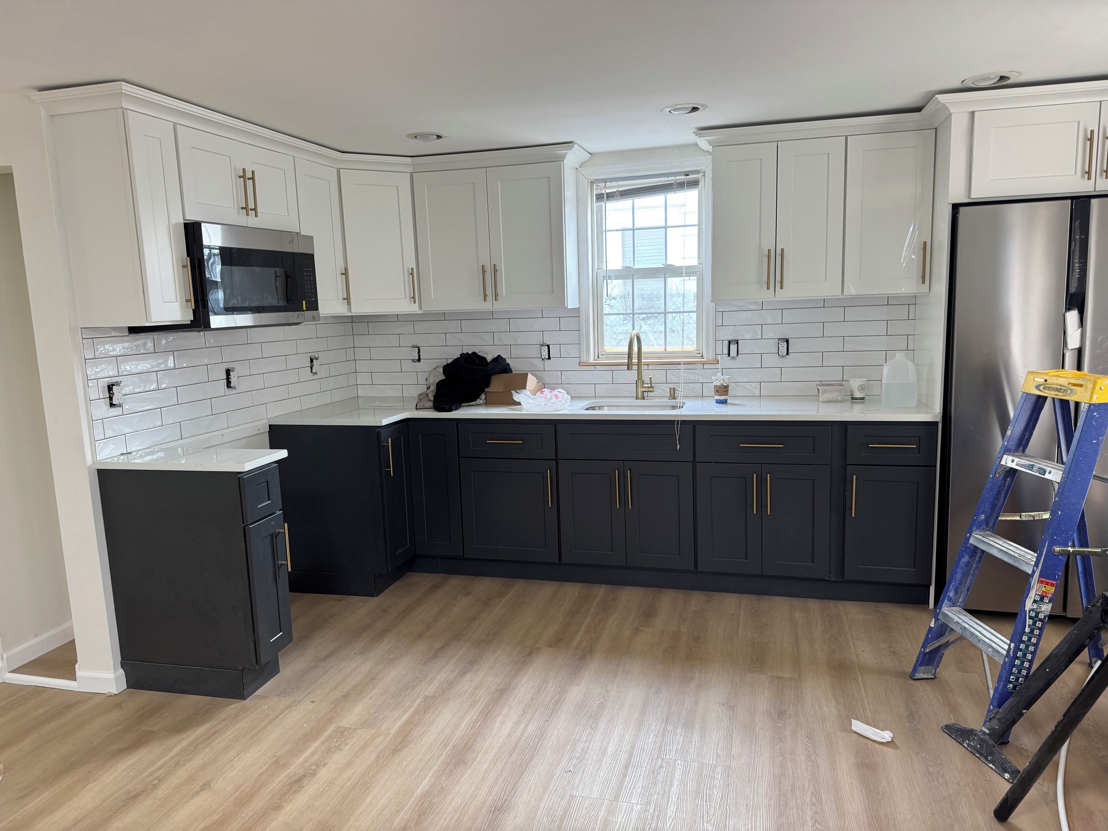 A kitchen with white cabinets, a black refrigerator, and a window.