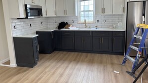 Una cocina con armarios blancos, un refrigerador negro y una ventana.