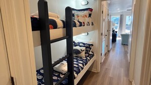 Een slaapkamer met stapelbedden, een houten vloer en witte muren. Er is een raam met uitzicht op het omliggende landschap.