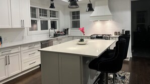 Una cucina moderna con mobili bianchi, un'isola centrale, lampade a sospensione nere e una orchidea rosa.