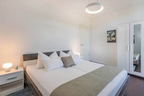 Een moderne hotelkamer met een groot bed, nachtkastjes, een garderobe en een plafondlamp.