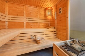Een houten sauna met banken, een emmer en een schaal met stenen.