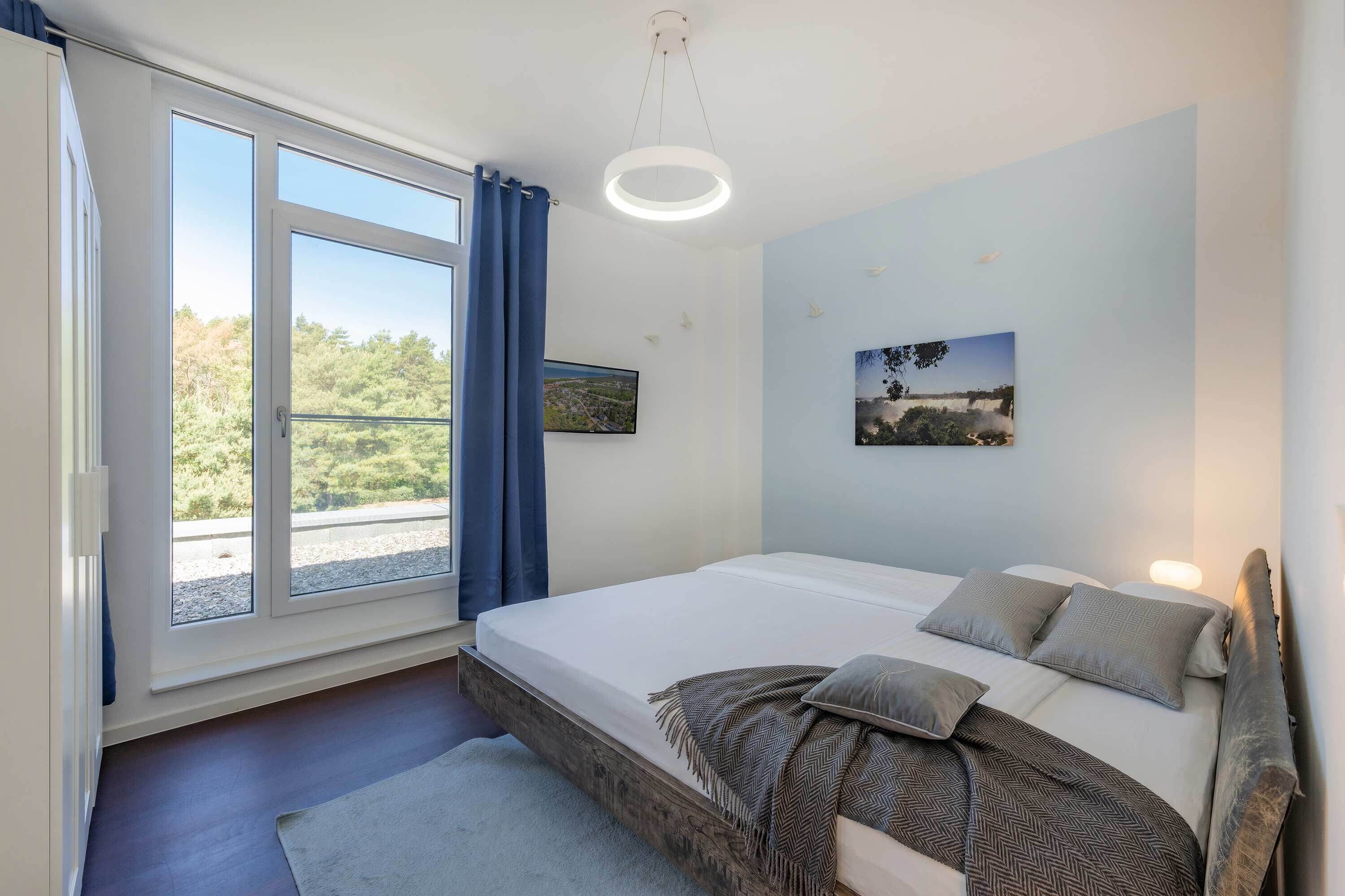 A bedroom with a bed, a window with curtains, a ceiling light, and a wall-mounted picture.