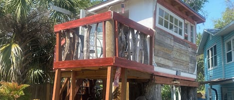 Ein Haus auf Stelzen mit einer Holzterrasse, umgeben von Bäumen und einer Hängematte.