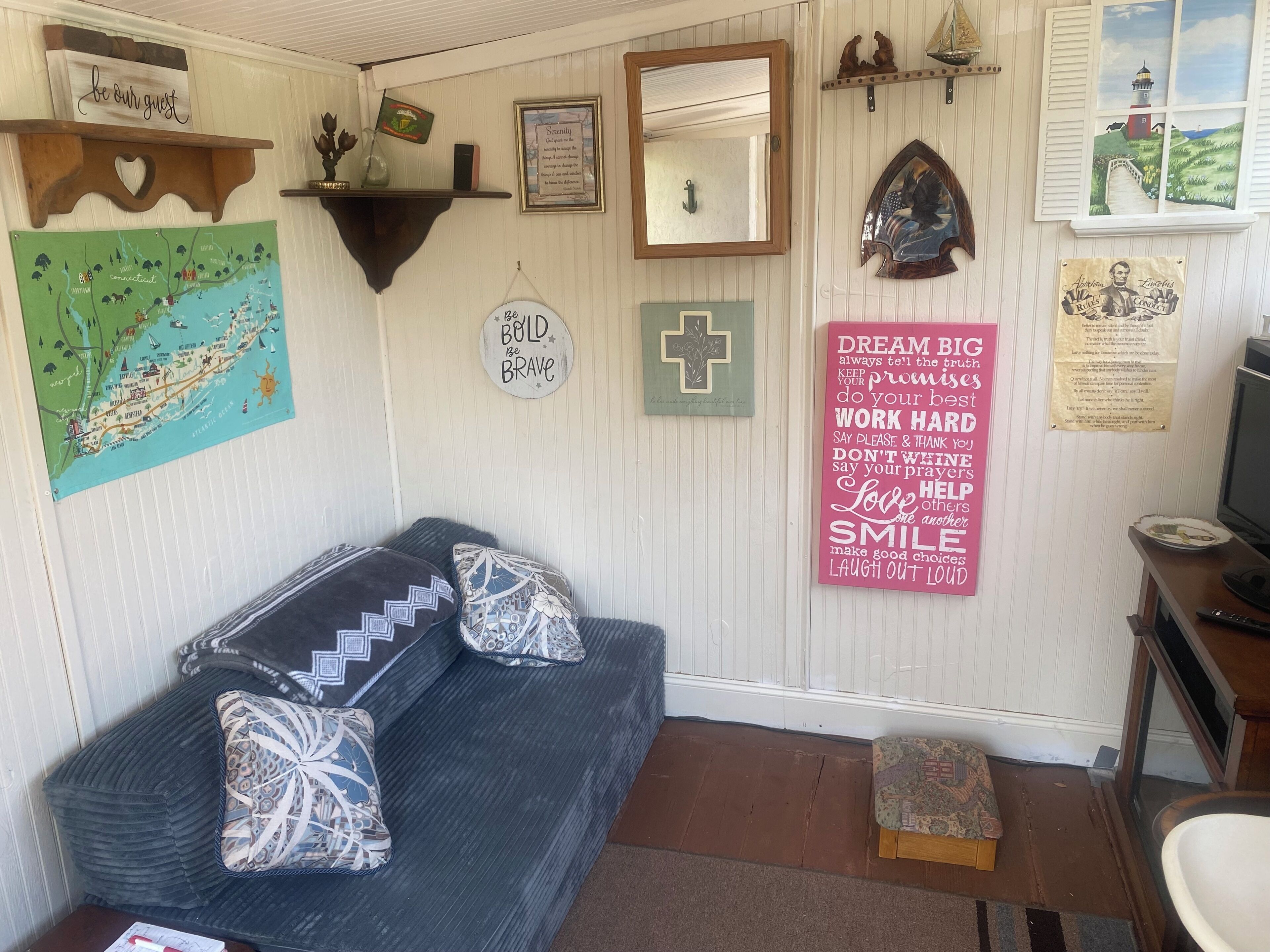 Una habitación acogedora con sofá, almohadas, un mapa, carteles motivacionales y una televisión.