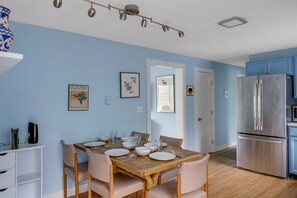 A modern kitchen with a stainless steel refrigerator, wooden dining table with chairs, and light blue walls.