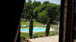 Udsigt gennem et vindue af en swimmingpool, liggestole og en træterrasse.