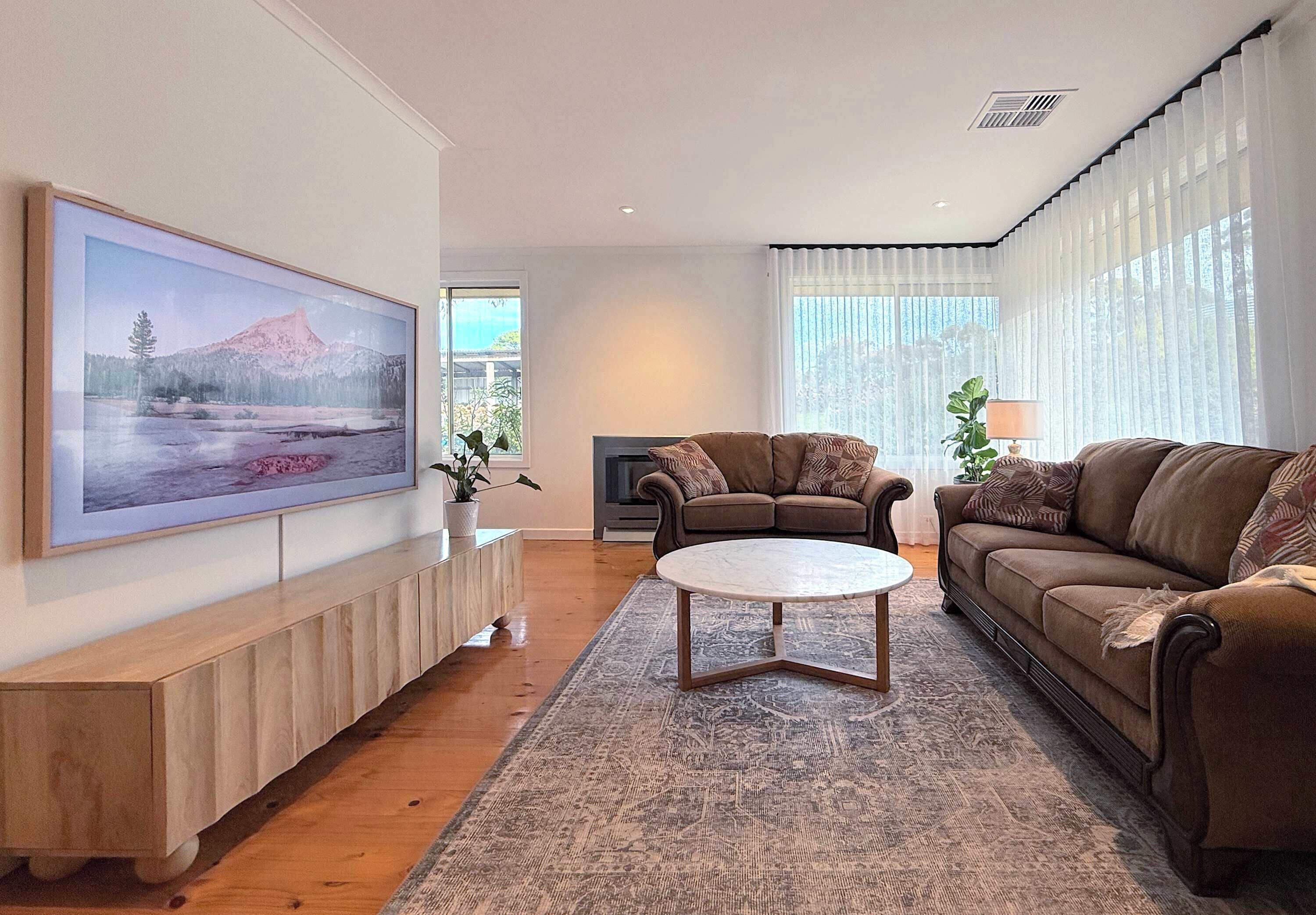 Ein Wohnzimmer mit einem großen Gemälde, einem braunen Sofa, einem runden Couchtisch und einem Kamin.