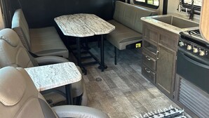 Interior compacto de uma RV com mesa de jantar, assentos, cozinha compacta e janela com a bandeira americana.