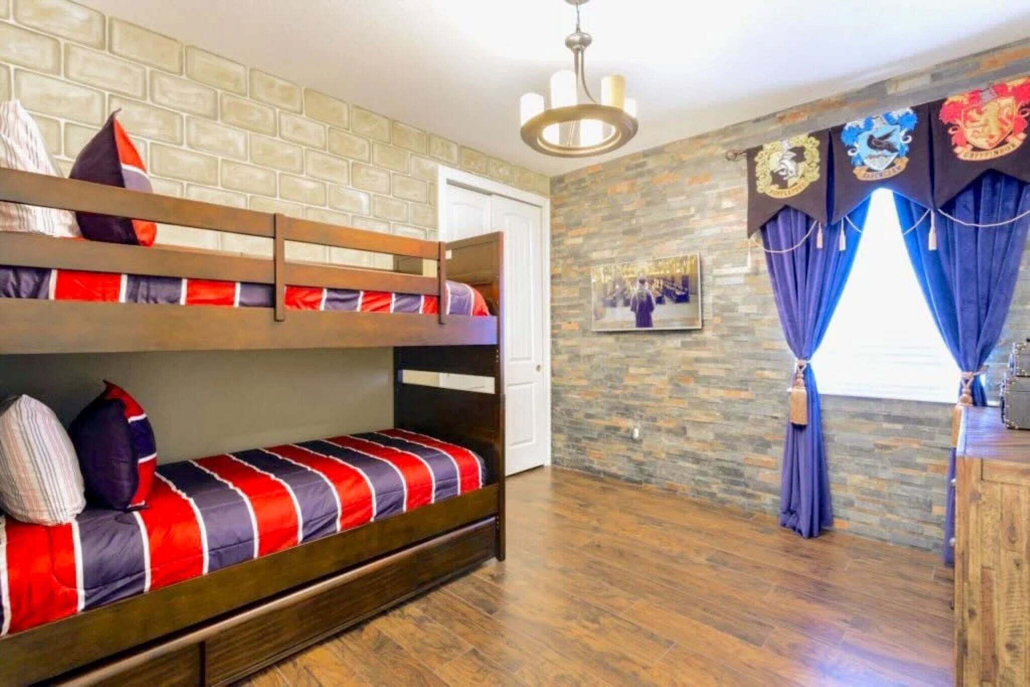 A room with a bunk bed, a stone wall, a wooden floor, and a window with curtains.