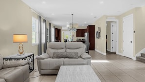 A spacious living room with a beige sofa, a coffee table, and a dining area in the background. - 7601 Luxury 7BR Themed Villa w/ Private Pool & Spa (Kissimmee)