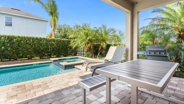 A pool area with a lounge chair, a table, and a grill. - 7601 Luxury 7BR Themed Villa w/ Private Pool & Spa (Kissimmee)