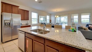 A spacious kitchen with granite countertops, a stainless steel refrigerator, and a large island with a sink. - 7BR Resort Pool Home Near Disney - 8004 (Davenport)
